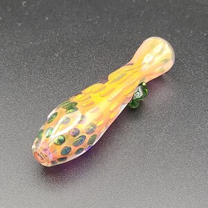 May include: A small, orange glass pipe with green and white speckles. The pipe is about 4 inches long and has a rounded end.