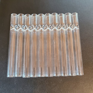 May include: A set of 12 clear glass smoking pipes, each approximately 4 inches long. The pipes are arranged in a row, with the ends of the pipes aligned.