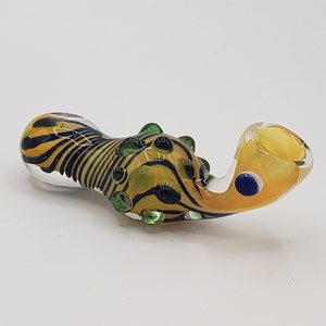 May include: A yellow and black striped glass pipe with green and blue accents. The pipe has a bulbous bowl and a curved mouthpiece.