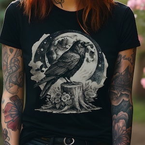 May include: A woman with long red hair is wearing a black t-shirt with a graphic of a crow perched on a tree stump in front of a full moon. The graphic is in black and white and has a vintage feel.