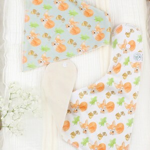 May include: Two baby bibs with a fox and acorn pattern. One bib is light blue with white foxes and the other is white with orange foxes. Both bibs have a white absorbent layer.