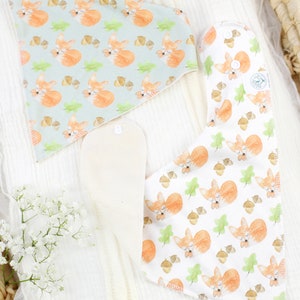 May include: Two triangular baby bibs with a fox and acorn pattern. One bib is light blue with white accents and the other is white with light green accents.