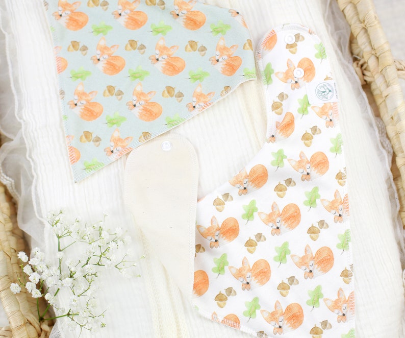 May include: Two triangular baby bibs with a fox and acorn pattern. One bib is light blue with white accents and the other is white with light green accents.