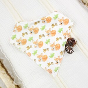 May include: A white bandana with a repeating pattern of sleeping foxes, acorns, and green leaves. The bandana is folded in a triangle shape and is lying on a white surface.