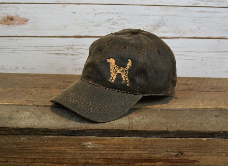 Może przedstawiać: Czapka bejsbolowa z ciemnozielonej tkaniny z haftowanym pomarańczowym sylwetem psa z przodu.