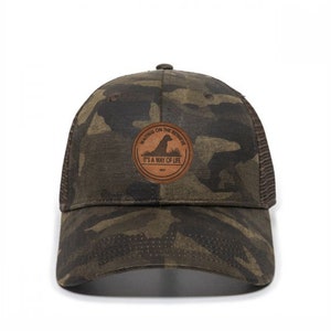 May include: A camouflage trucker hat with a brown leather patch that says "Waiting on the Retrieve, It's a Way of Life".