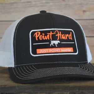 May include: Black and white trucker hat with a black and orange patch that says "Point Hard" with a white silhouette of a dog and the text "Just Point Mania".