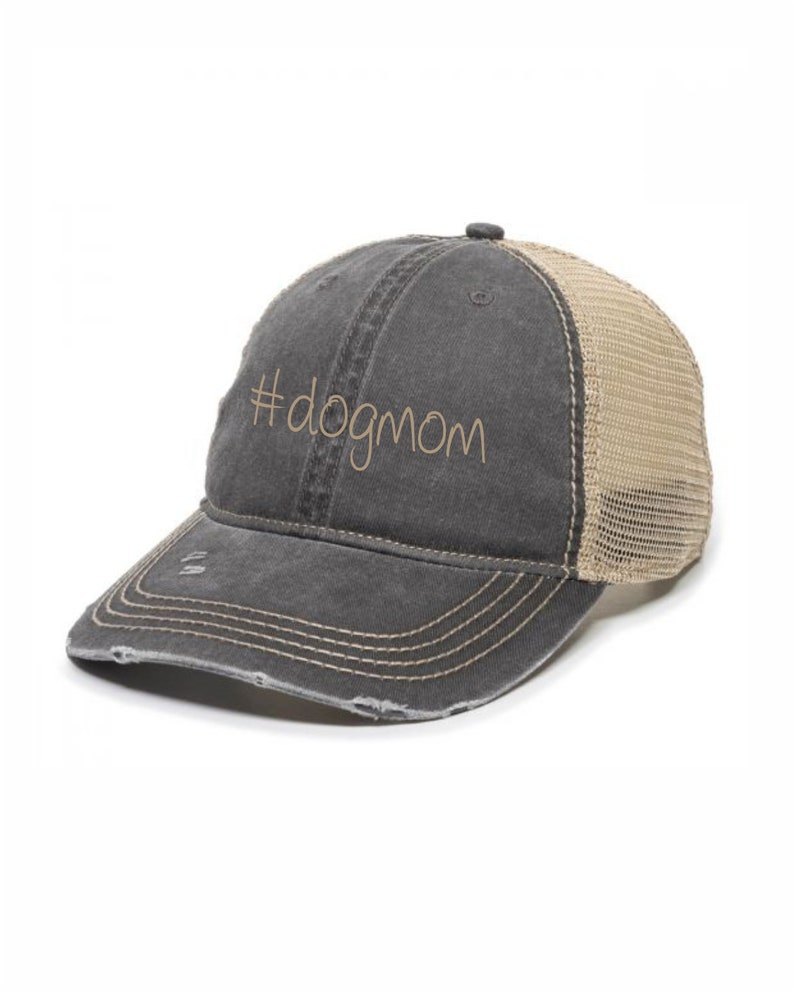 Peut inclure: Un chapeau de camionneur en toile d&eacute;lav&eacute;e noir et beige avec un dos en mesh. Le chapeau a le texte "#dogmom" brod&eacute; sur le devant.