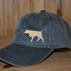 Może przedstawiać: Czapka z daszkiem w ciemnoszarym kolorze z haftowanym brązowym siluetką psa z przodu.