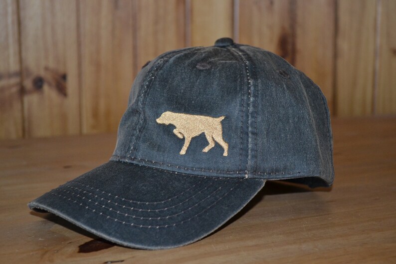 Może przedstawiać: Czapka z daszkiem w ciemnoszarym kolorze z haftowanym brązowym siluetką psa z przodu.