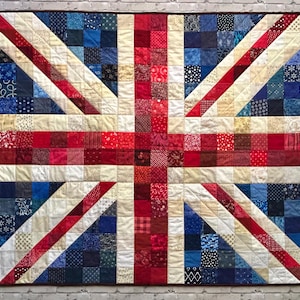 May include: A handmade quilt depicting the Union Jack flag. The quilt features a patchwork design with red, white, and blue fabrics. The flag's cross and diagonal stripes are prominently displayed, with a variety of patterns and textures within each color section.
