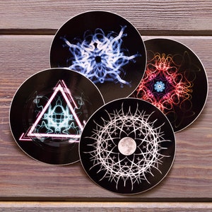 May include: Four round stickers with different abstract designs. The stickers are black with white, blue, and red designs. The designs are geometric and abstract.