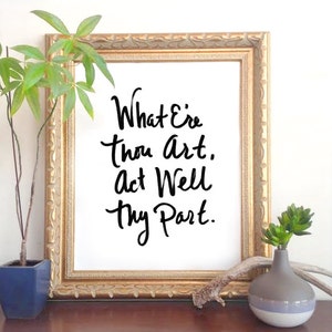 Op de afbeelding: Een ingelijst afdruk met een gouden lijst en een witte achtergrond. De afdruk bevat zwarte kalligrafie met de tekst "What E're thou art. Act Well thy Part."