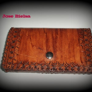 May include: A brown leather wallet with a decorative embossed design and a silver button closure. The wallet has a stitched border.