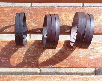 May include: Three brown leather bracelets with silver snap closures. The bracelets are stacked on top of each other on a wooden surface.
