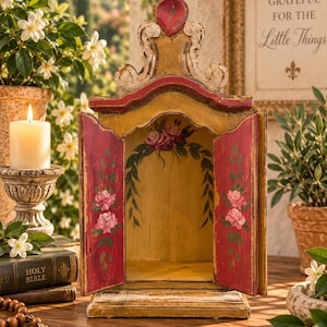 Puede incluir: Un santuario de madera con parte superior arqueada, con un acabado desgastado en amarillo y rojo. El interior y las puertas están decorados con rosas rosas y follaje verde pintados a mano. La estructura tiene dos puertas abatibles.