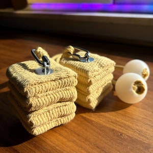 Op de afbeelding: Twee sets gele stoffen vuurpoi met een zilveren metalen lus en een witte gewogen bal bevestigd aan elke set.