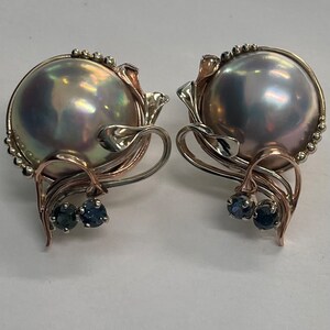 May include: A pair of silver and rose gold earrings with a large iridescent pearl and two small blue sapphires.