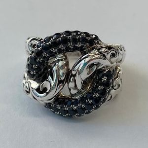 May include: A silver ring with a black stone design. The ring is made of a twisted metal band with a black stone design. The ring is a statement piece and would be a great addition to any jewelry collection.