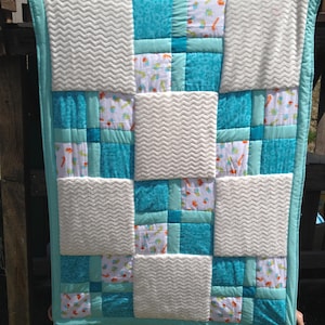 May include: A turquoise and white patchwork baby quilt with a variety of patterns, including zigzags, polka dots, and animal prints.