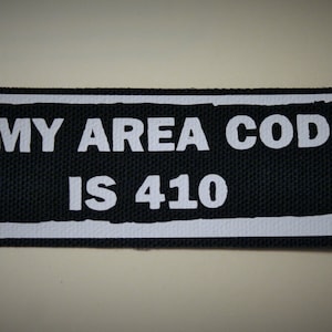 May include: Black and white fabric patch with the text "MY AREA CODE IS 410" in a white rectangle.