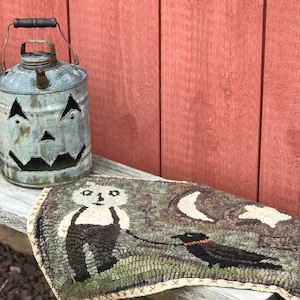 May include: A vintage metal jack-o'-lantern with a rustic patina sits on a wooden surface next to a hand-stitched wool rug with a whimsical design featuring a bear and a bird.