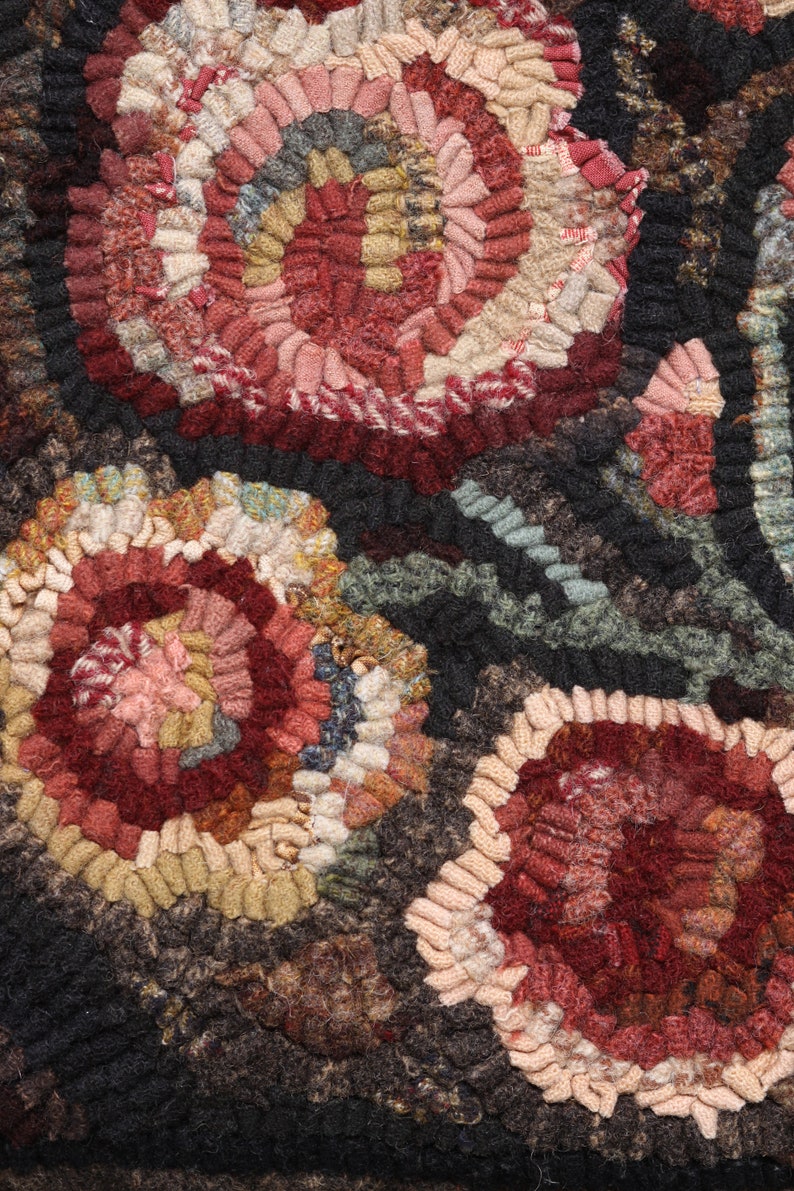 May include: Close-up of a handmade rug with a floral design. The rug features a variety of colors, including red, pink, beige, and green, arranged in a circular pattern. The background is a dark brown color.