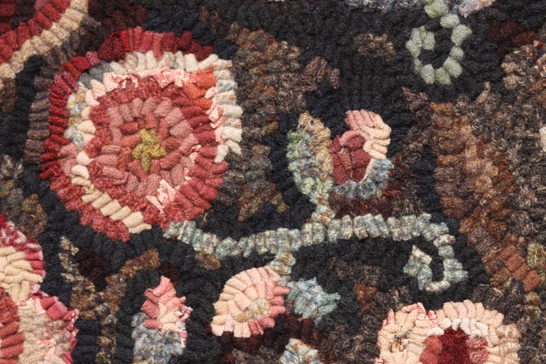May include: Close-up of a handmade rug with a floral pattern. The rug features a dark background with colorful, textured flowers in shades of red, pink, and beige. The design is intricate and detailed, showcasing the craftsmanship.