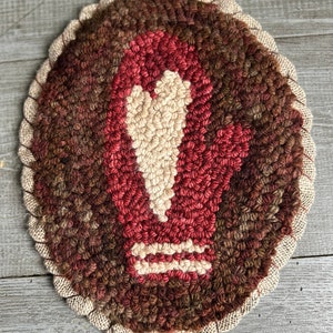 May include: A hand-stitched wool rug with a brown, red, and cream color scheme. The rug features a stylized arrow design in the center.
