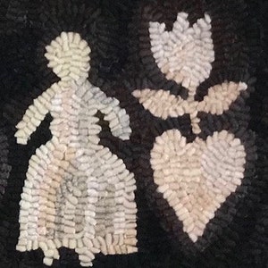 May include: A handmade rug with a black background features a white figure of a person, a tulip, and a heart. The figures are made of small, textured pieces, creating a unique, folk art style. The rug is likely made of wool or a similar material.