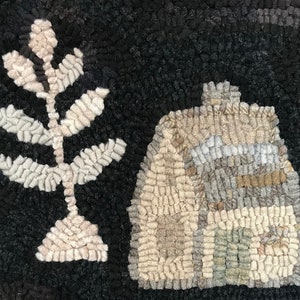 May include: A handmade rug with a black background features a stylized house and a leafy plant. The house is beige, gray, and green, while the plant is beige and white. The rug's texture is visible, adding depth to the design.