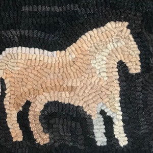 May include: A hand-hooked rug featuring a horse silhouette. The horse is rendered in shades of tan, cream, and white against a dark gray and black background. The rug's texture is visible, showcasing the looped yarn construction.