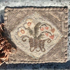 May include: A brown and beige hooked rug with a floral design. The rug features a basket of flowers with pink, white, and green accents.