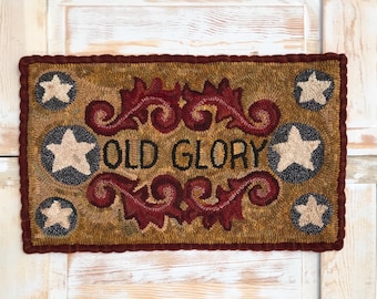May include: A brown and tan rug with a red and white floral design and the words "Old Glory" in black. The rug is surrounded by a red border and has white stars in the corners.