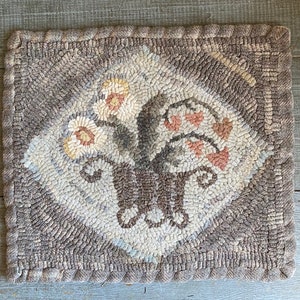May include: A hand-hooked rug with a floral design in shades of brown, beige, and pink. The rug has a diamond-shaped center with a floral motif and a border of brown and beige.