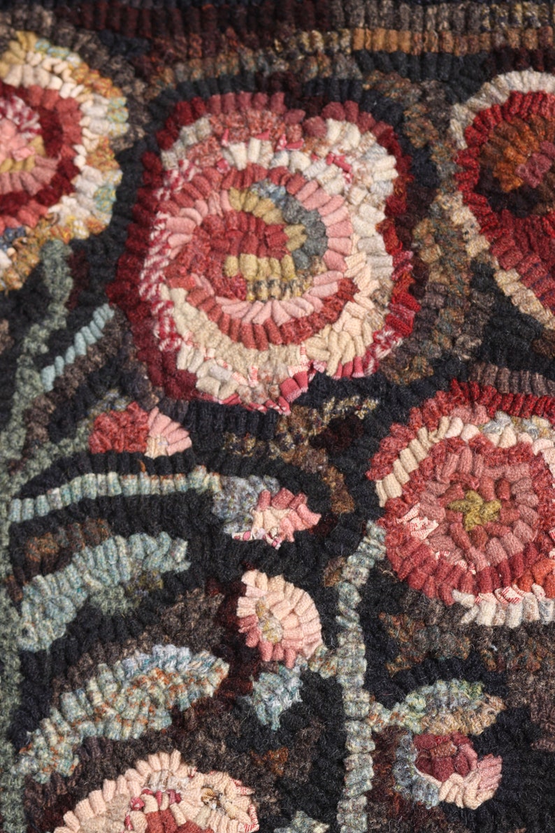May include: Close-up of a handmade rug with a floral design. The rug features large, stylized flowers in shades of red, pink, and cream against a dark background. The texture is created with looped yarn, giving a three-dimensional effect.