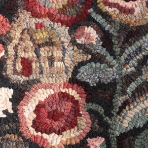 May include: Close-up of a handcrafted rug with a floral design. The rug features a repeating pattern of large, stylized flowers in shades of red, pink, and cream, set against a dark background. The texture is thick and looped, suggesting a durable, handmade item.