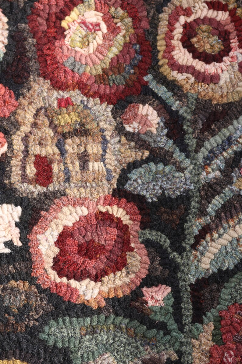 May include: Close-up of a handcrafted rug with a floral design. The rug features a repeating pattern of large, stylized flowers in shades of red, pink, and cream, set against a dark background. The texture is thick and looped, suggesting a durable, handmade item.