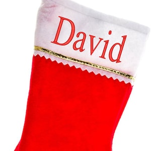 May include: A red Christmas stocking with a white cuff and a gold trim. The name "David" is embroidered in red on the cuff. A red loop is attached to the top for hanging. Festive holiday decor.