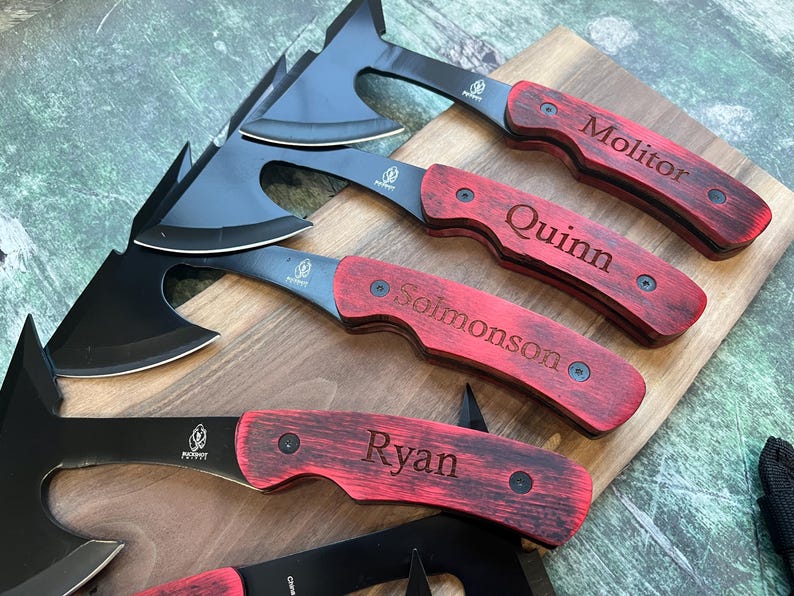 May include: Four personalized black and red hatchet knives with wooden handles. The handles are engraved with the names "Ryan", "Solomonson", "Quinn", and "Molitor".