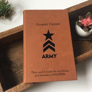 May include: A brown leather journal with the name "Gregory Connor" and the word "ARMY" printed on the front. The journal also has a black star and chevron design and the text "They said I could do anything, so I became a SOLDIER."