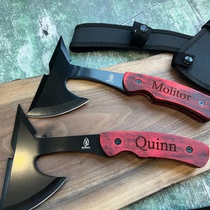 May include: Two black throwing axes with red wooden handles. The handles are engraved with the names "Molitor" and "Quinn".