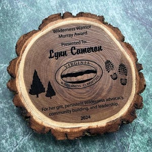 May include: A wooden plaque with the text "Wilderness Warrior Murray Award Presented To: Lynn Cameron VIRGINIA WILDERNESS COMMITTEE For her grit, persistent Wilderness advocacy, community building, and leadership. 2024"