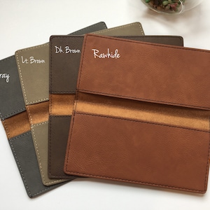 May include: Four rectangular checkbook covers arranged in a fan shape, featuring colors labeled as Gray, Lt. Brown, Dk. Brown, and Rawhide. Each cover has visible stitching along the edges and a contrasting smooth interior strip across the center.