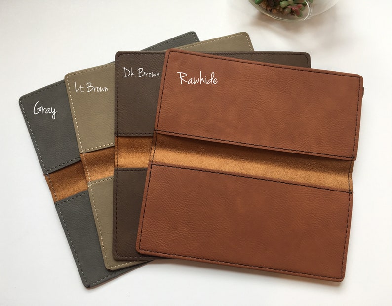 May include: Four rectangular checkbook covers arranged in a fan shape, featuring colors labeled as Gray, Lt. Brown, Dk. Brown, and Rawhide. Each cover has visible stitching along the edges and a contrasting smooth interior strip across the center.