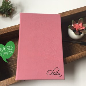 Puede incluir: Un diario de cuero rosa con el nombre "Olivia" grabado en la portada. El diario est&aacute; en una caja de madera con una pegatina verde en forma de coraz&oacute;n que dice "Muchos estilos para elegir".