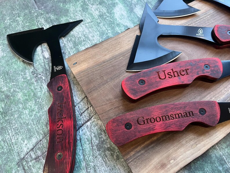 May include: A set of three personalized pocket knives with black blades and red wooden handles. The handles are engraved with the words "Usher", "Groomsman", and "Jackson".