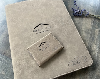 May include: A gray leather-bound journal with the text "CGR Realty Group Love Where You Live" and a matching business card holder with the same text and the name "Chris R." embossed on it.
