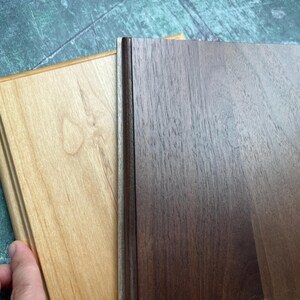 May include: Two wooden plaques, one light-colored and one dark, are displayed. The light plaque has a natural wood grain and a decorative edge. The dark plaque has a rich, brown color and a smooth surface. The plaques are side by side.