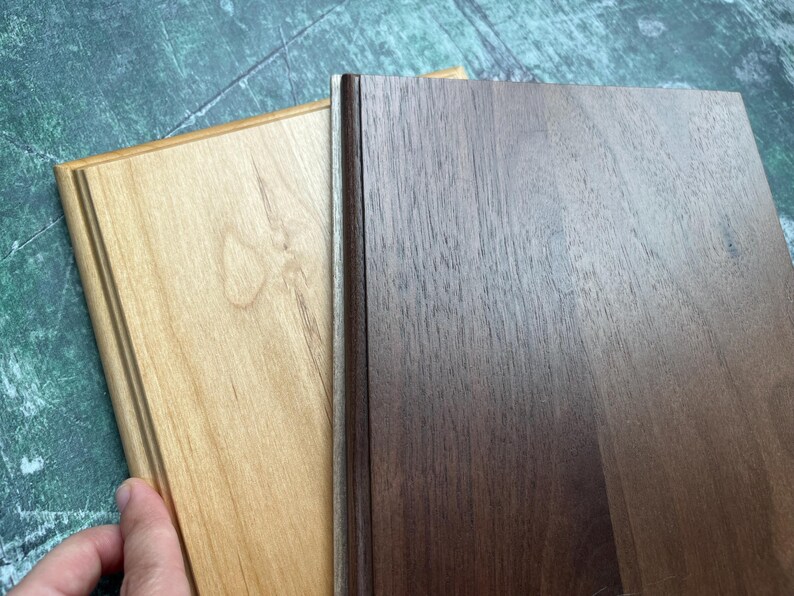 May include: Two wooden plaques, one light-colored and one dark, are displayed. The light plaque has a natural wood grain and a decorative edge. The dark plaque has a rich, brown color and a smooth surface. The plaques are side by side.